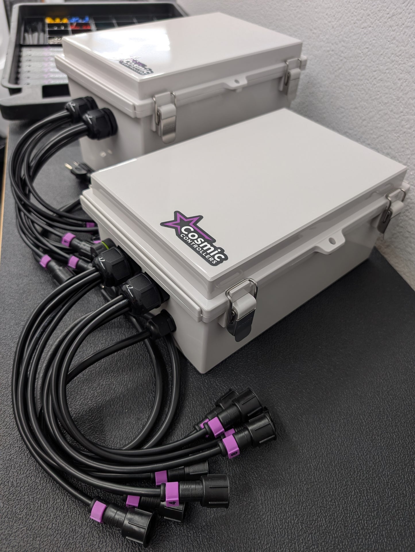 Two Cosmic Controllers gray waterproof plastic pixel controller enclosures with black electrical cables coming out of them.