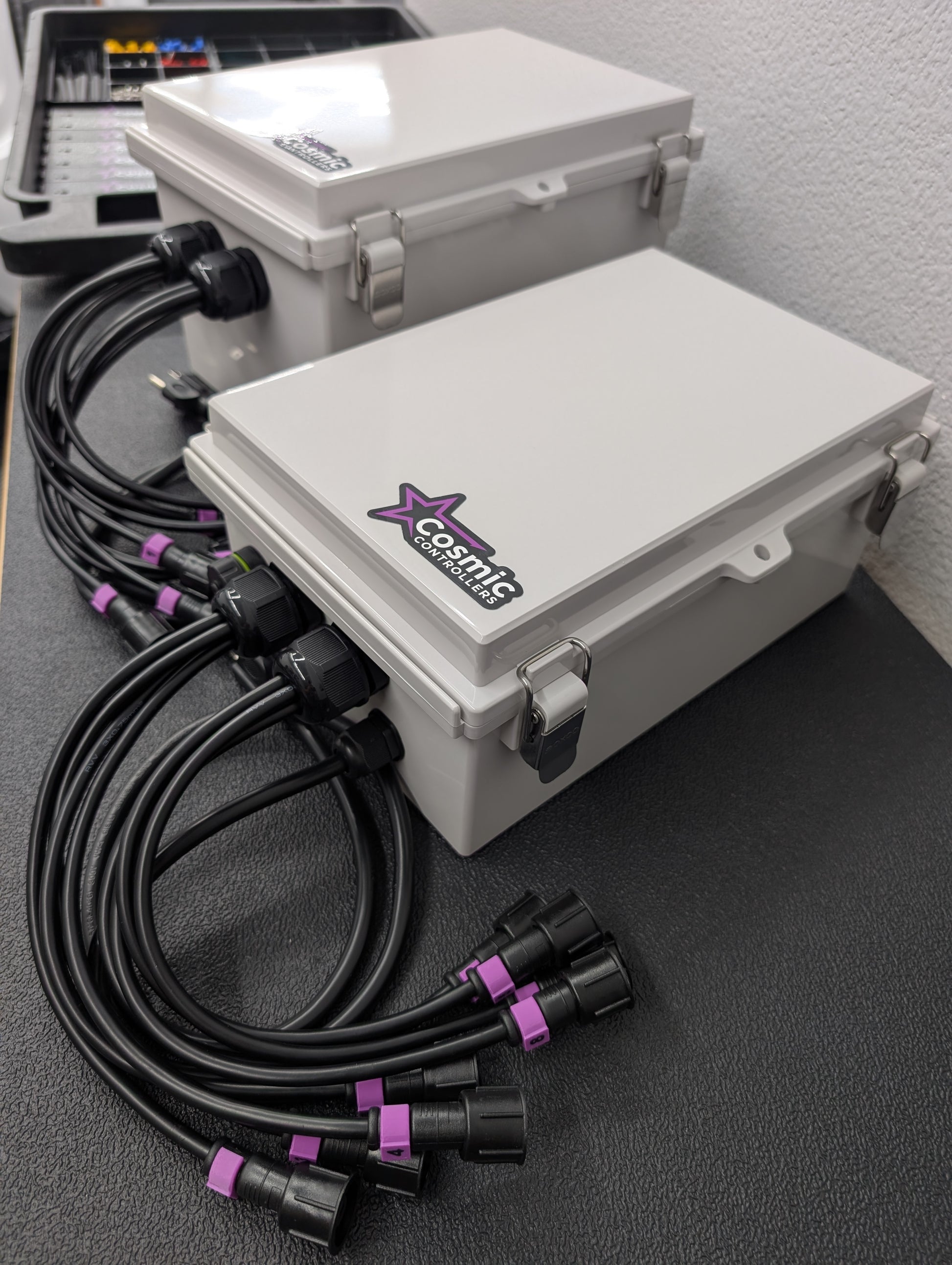 Two Cosmic Controllers gray waterproof plastic pixel controller enclosures with black electrical cables coming out of them.