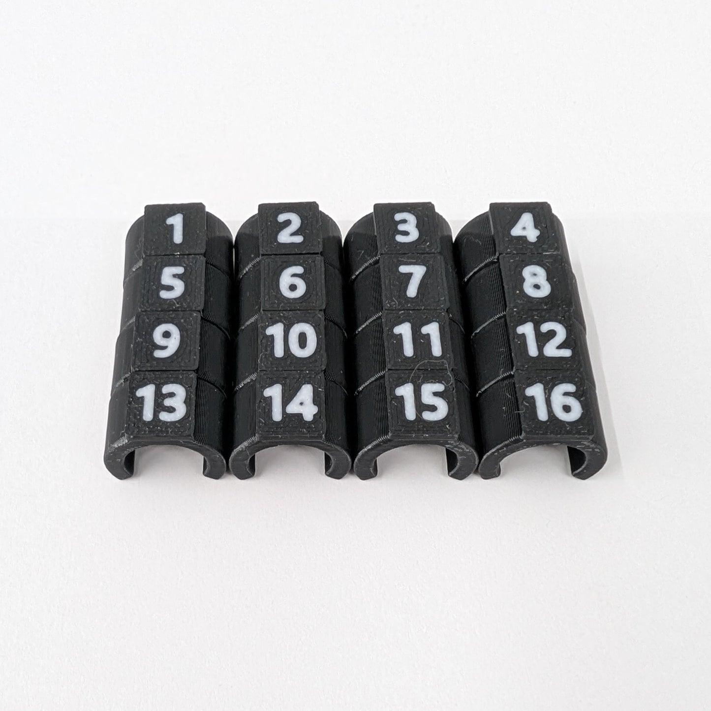 Close-up of black cable ID clips with white numbers 1-16 on a white background