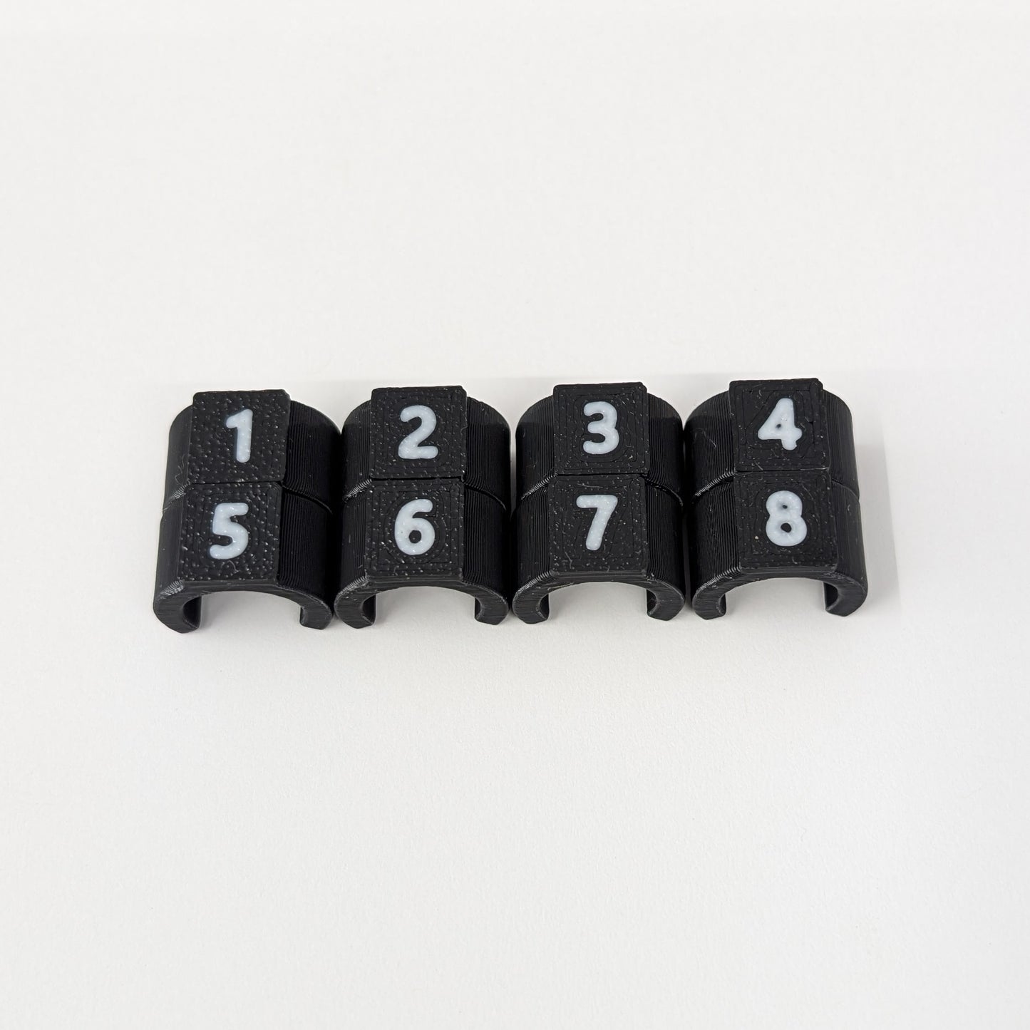 Close-up of black cable ID clips with white numbers 1-8 on a white background